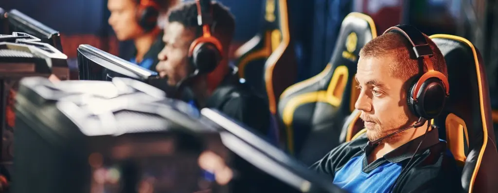 Een toegewijd team van esports-spelers met headsets gaat in een slecht verlichte gamingarena een intense strijd aan op computers, waarbij teamwork en concentratie centraal staan